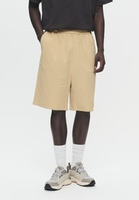 Beige shorts with an elastic waistband, made from textured fabric. Paired with gray sneakers and white crew socks.