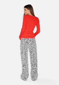 Rotes geripptes Langarmoberteil, kombiniert mit hoch taillierten weit geschnittenen Hosen im schwarz-weißen Zebra-Druck, die einen entspannten Schnitt und eine glatte Textur zeigen.