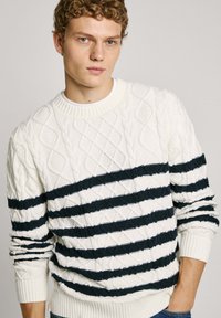 Pull en maille blanche avec des rayures horizontales navy, col rond et poignets côtelés. La texture est épaisse et texturée.