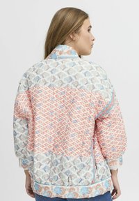 Giacca trapuntata caratterizzata da un mix di motivi geometrici e floreali in colori corallo, blu e crema, con una vestibilità comoda e polsini a costine.