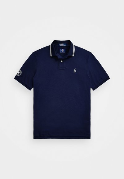 Ναυτικό μπλε πόλο μπλουζάκι από βαμβάκι, με τριπλό κουμπί, λευκή ριγέ γιακά, κοντά μανίκια, και κεντημένο λογότυπο στο στήθος.