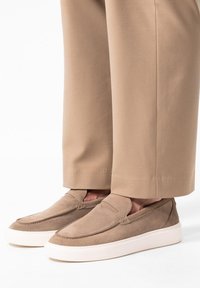 Beige Wildlederschuhe mit einem Slipper-Design und weißen Gummisohlen, die über dezente Nähte und eine abgerundete Spitze verfügen. Die Hose ist khaki.