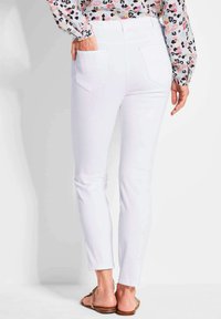 Witte jeans met een slim fit, voorzien van achterzakken en een gladde textuur. Draagt met een bloemenpatroon top en sandalen.