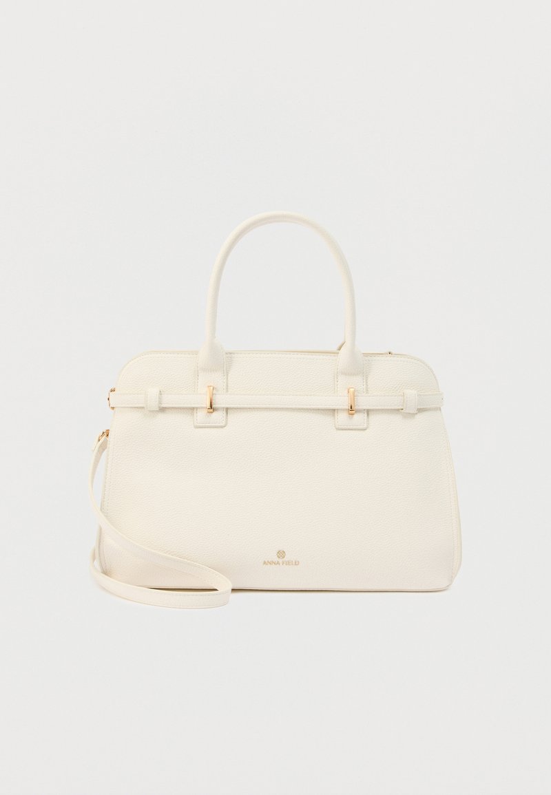 Sac à main en cuir texturé de couleur crème avec double poignée, bandoulière amovible et logo "ANNA FIELD" doré sur le devant.