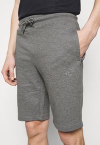 Šedé šortky ze směsi bavlny s elastickým pasem a stahovací šňůrkou. Mají boční kapsy a diskrétní logo na levém stehně.