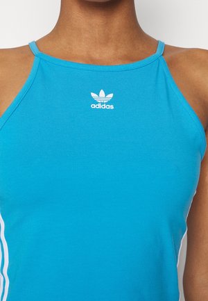 Zbliżenie osoby noszącej niebieski top na ramiączkach Adidas z cienkimi paskami i białym logo Adidas trefoil na środku klatki piersiowej.