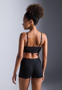 Svart ribbet sport-bralett med justerbare stropper og matchende shorts, vist på en modell som viser en bakutsikt mot en nøytral bakgrunn.