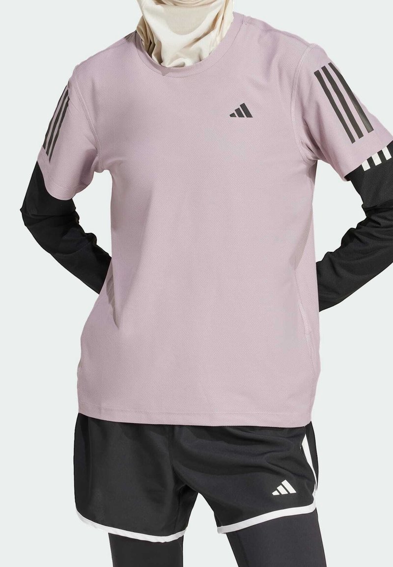 Ljusrosa sporttshirt med svarta långa ärmar, med ett texturerat tyg och tre svarta ränder på varje axel. Svarta shorts med vit kant.