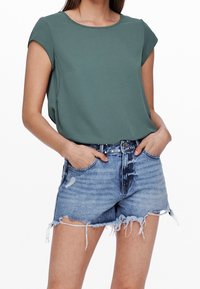 Haut vert foncé à manches courtes avec un col rond, associé à un short en denim bleu clair déchiré avec des bords effilochés et des poches.