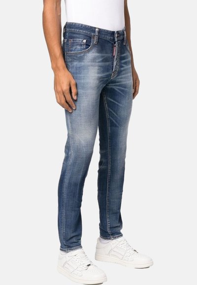 Jeans de denim azul desgastado con corte slim, que cuentan con cinco bolsillos y costuras en contraste. Combinados con zapatillas blancas.