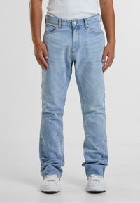 Lys blå denim jeans med rette ben, fem-lomme-design og synlige sømmer. Brukt med en hvit tank topp og hvite sneakers.