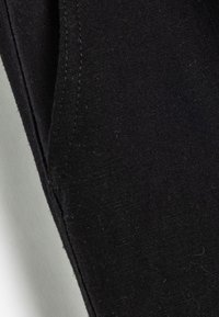 Zwarte katoenstof met een gladde textuur, met zichtbare stiksels langs de randen en naden. Geen duidelijke patronen of accenten.