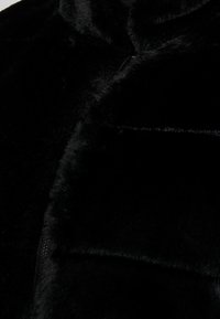 Chaqueta de piel sintética negra con un acabado suave y texturizado, que cuenta con un cierre de cremallera y un bolsillo. El diseño incluye un cuello alto.