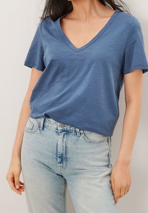 Kortærmet t-shirt med v-hals i et blødt blåt stof, der har en afslappet pasform og let struktur. Parret med lyseblå denimjeans.