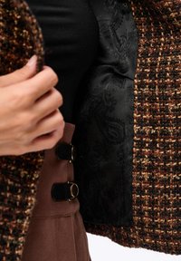Tweed-Jacke mit einer braun-schwarzen strukturierten Außenseite, ausgestattet mit einem glatten schwarzen Paisleymuster-Futter und goldfarbenen Hardware-Akzenten.