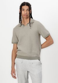 Polo de malha de manga curta, verde claro, com um design texturizado, gola e bainha caneladas. Usado com calças cinza claro, com cordão.