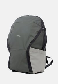 Groene rugzak met een grijs ondergedeelte, gemaakt van duurzaam materiaal. Beschikt over een zijvak, ritsafsluiting en zwarte accenten. Gladde textuur.