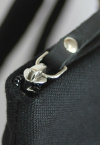 Schwarze Stofftasche mit einem Reißverschluss, der einen silbernen Metallreißverschluss-Zipper und eine strukturierte Oberfläche aufweist. Nahaufnahme zeigt die Details des Reißverschlusses.