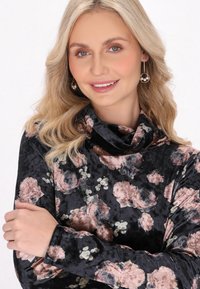 Ylppäritakki mustassa veluurissa kukkakuosisella printillä, jolla on kauniisti laskeutuva kaula-aukko. Siinä on vaaleanpunaisia ja valkoisia kukkia, pehmeä pinta ja pitkät hihat.