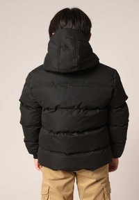 Doudoune noire avec capuche, présentant un design matelassé et une finition texturée. La doudoune a une coupe ajustée et une longueur mi-saison.