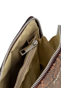 Interno della borsa a tracolla marrone intrecciata con fodera in tessuto beige, tasca con zip e hardware in metallo, e una zip liscia lungo l'apertura.