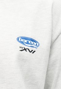 Λευκό ύφασμα με μπλε οβάλ λογότυπο που γράφει "barcen" και μαύρο κείμενο από κάτω που αναγράφει "MM XVI" σε διπλωμένο ένδυμα.