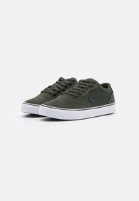 Grønne suede sneakers med hvide gummisåler, snørebånddesign, kontrasterende sort logo på siden og en lav profil.