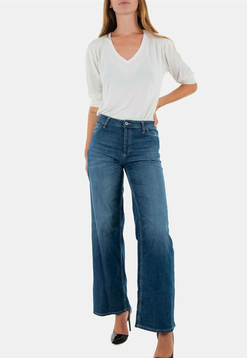 Jeans de denim azul de cintura alta con un corte relajado y piernas anchas. Combinados con una camiseta blanca de cuello en V y tacones negros puntiagudos.