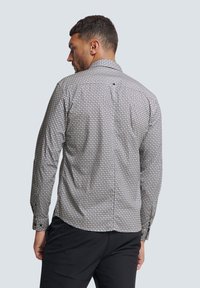 Langarmshirt in een gemusterde stof, met geometrische ontwerpen in blauw en beige. De achterkant toont een knoopsluiting bij de nek.