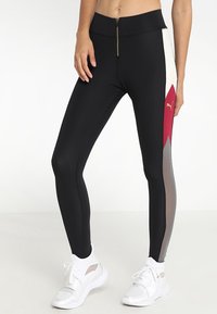 Leggings neri con vita con cerniera, caratterizzati da pannelli rossi, crema e grigi. Realizzati in tessuto elasticizzato, progettati per l'abbigliamento sportivo.