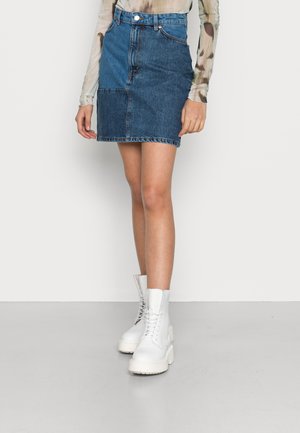 Saia mini de ganga com um design em retalhos em azul escuro e claro, de cintura alta, com bainha desfiada, combinada com botas de cano curto brancas com plataforma.