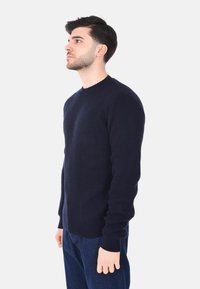 Maglione a coste di colore blu navy con scollo rotondo e maniche lunghe, esposto su un modello di lato su uno sfondo bianco.