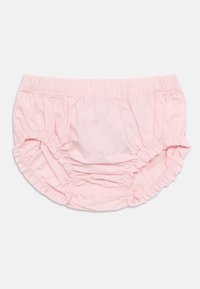 Shorts bloomers en coton rose avec ceinture élastique et bords volantés. Texture douce, coupe ample et détails froncés sur les côtés.