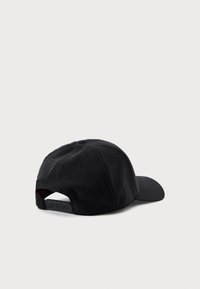 Svart caps laget av myk, teksturert stoff med en buet skjerm. Har logo bak og ventilasjonsluker. Justerbar stropp bak.