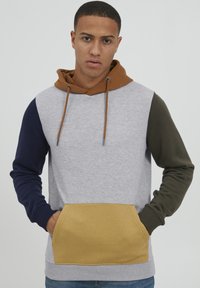 Farbenblockierter Kapuzenpullover mit hellgrauem Körper, navyblauen und olivgrünen Ärmeln, braunem Kapuze und einer senfgelben Fronttasche. Weicher Stoff.