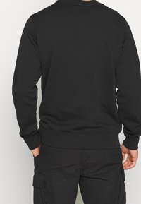 Sweatshirt noir à manches longues, avec des poignets et un ourlet côtelés. Fabriqué dans un matériau lisse, présentant un design simple et uni.