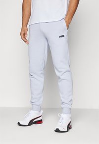 Light blue jogger pants with elastic cuffs, side pockets, and a black Puma logo on the left hip. Worn with white sneakers featuring red accents.