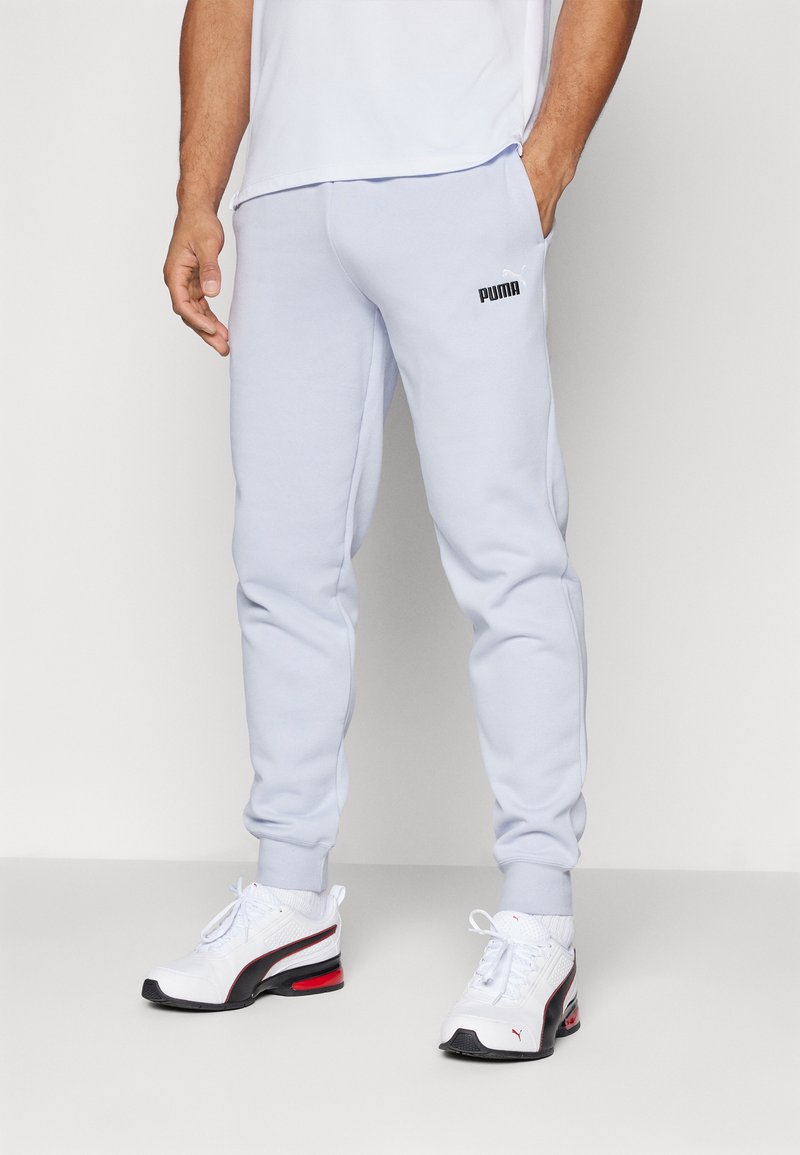 Light blue jogger pants with elastic cuffs, side pockets, and a black Puma logo on the left hip. Worn with white sneakers featuring red accents.
