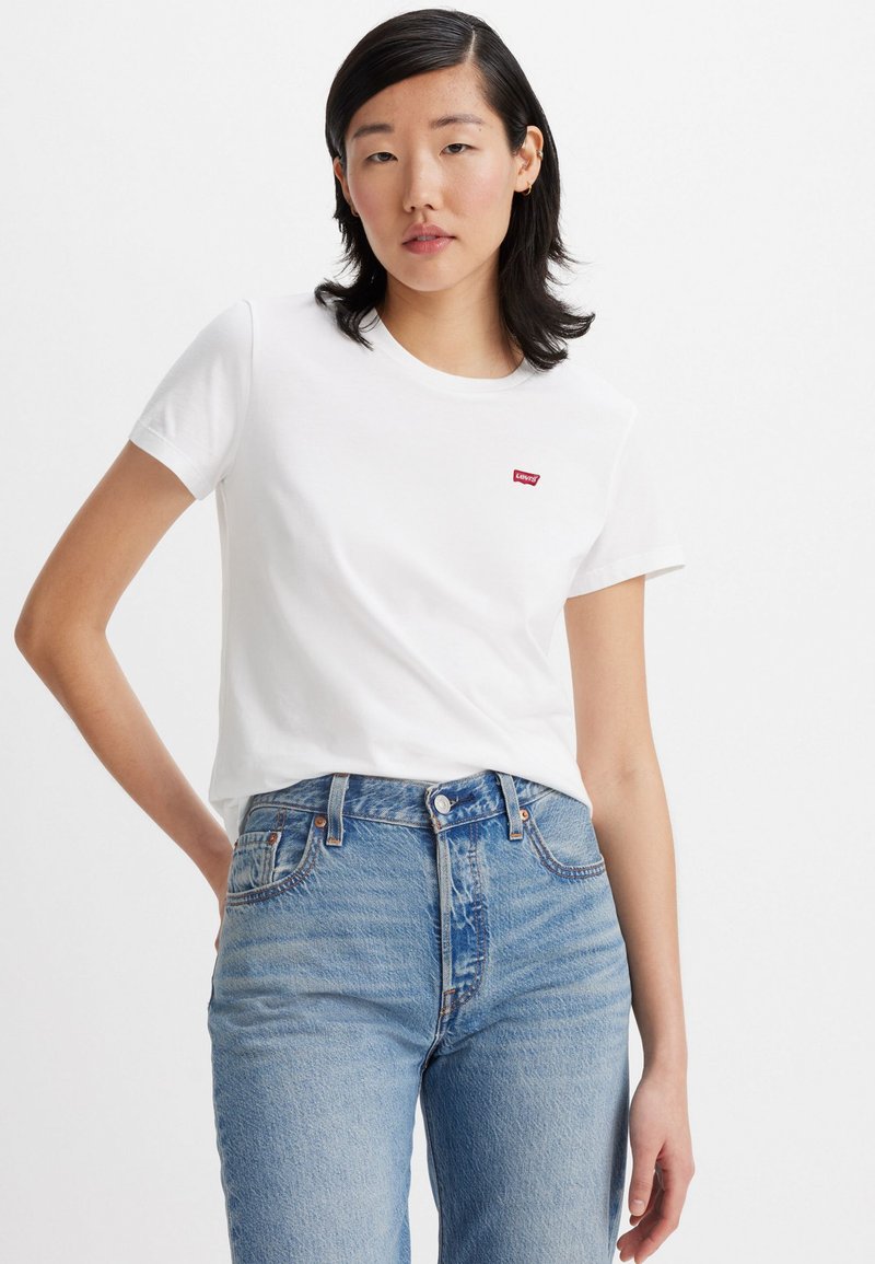 Camiseta de algodón blanca de manga corta con un pequeño logo rojo de Levi's en el pecho, combinada con unos vaqueros de cintura alta en azul claro.