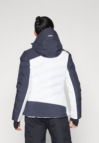 Gefütterte Winterjacke mit taillierter Passform. Farbkombination in Marineblau und Weiß, ausgestattet mit einer Kapuze und elastischen Bündchen mit Daumenlöchern. CMP-Logo angezeigt.