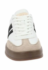 Zapatilla blanca con rayas negras, punta de gamuza beige y suela de goma marrón. Presenta cordones blancos y una parte superior texturizada.