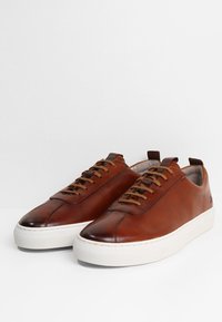 Braune Leder Sneakers mit glatter Oberfläche, runde Zehenpartie, weiße Gummisohle und braune Schnürsenkel. Einfaches Design mit minimalen Akzenten.