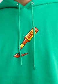 Grøn hættebluse med et ketchupflaske grafik, der har "NIKE!" i gul og rød. Stoffet er struktureret; snoretrækkene er fastgjort med metalspidser.