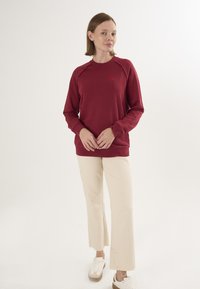 Bordowy sweatshirt z rękawami raglanowymi, z małym szczegółem w postaci czerwonego serca. W połączeniu z kremowymi spodniami z szerokimi nogawkami i białymi trampkami.