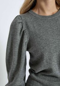 Pullover grigio lavorato a maglia con scollatura rotonda e maniche a sbuffo. Il tessuto sembra morbido con una texture liscia e una leggera lucentezza.