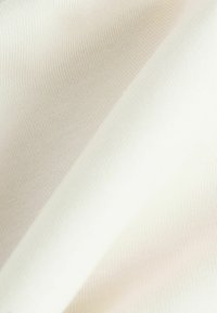 Tissu doux de couleur crème clair, présentant une texture lisse et un léger extensibilité. Le tissage affiche un motif fin et régulier.
