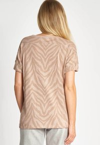 Beiges T-Shirt mit kurzen Ärmeln und einem dezenten Zebramuster. Hergestellt aus weichem Material, mit lockerem Schnitt und umgeschlagenen Ärmelsäumen.