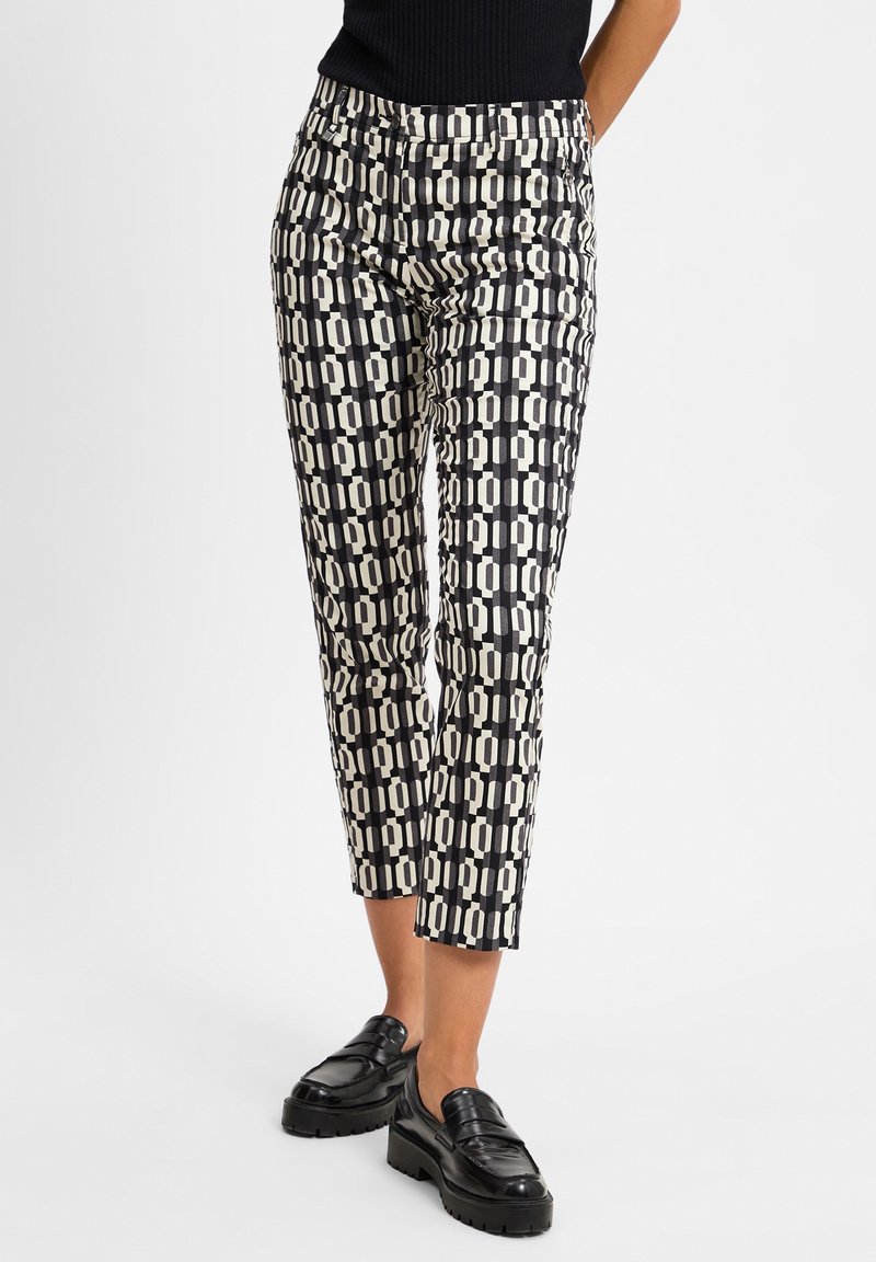 Pantalones negros y crema con un diseño geométrico, de corte slim, longitud cropped y una textura suave, combinados con mocasines negros.