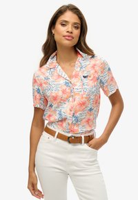 Koszula z krótkim rękawem i kołnierzykiem w kolorze białym z kwiatowym wzorem, zawierającym różowe i pomarańczowe kwiaty hibiskusa, niebieskie akcenty oraz małe logo.