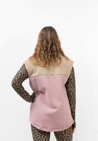 Fleece-Weste mit pinkem Körper, beigem Schulterbereich und Ärmeln mit schwarzem Leopardenmuster. Weiche Textur und ärmelloses Design.